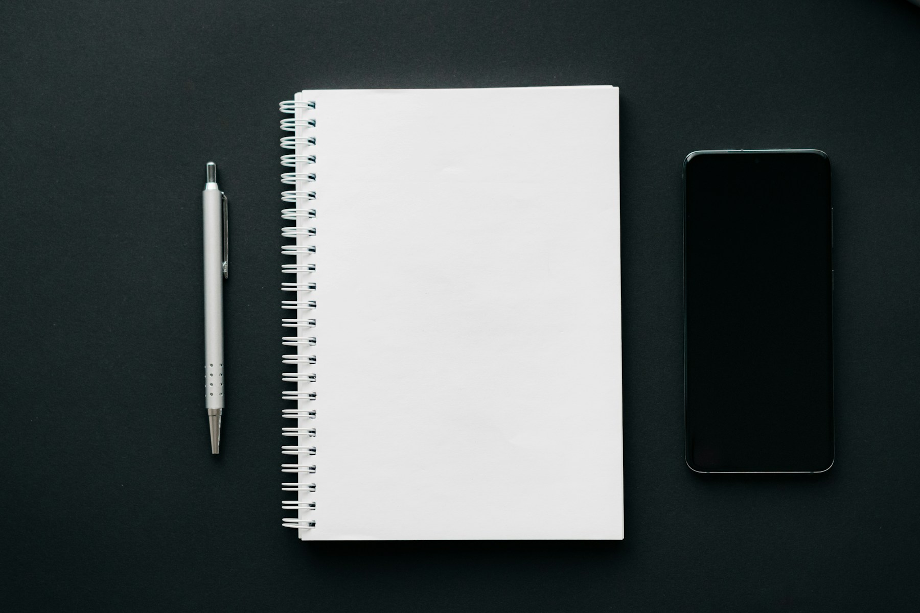 A silver pen and blank notebook on a dark desk